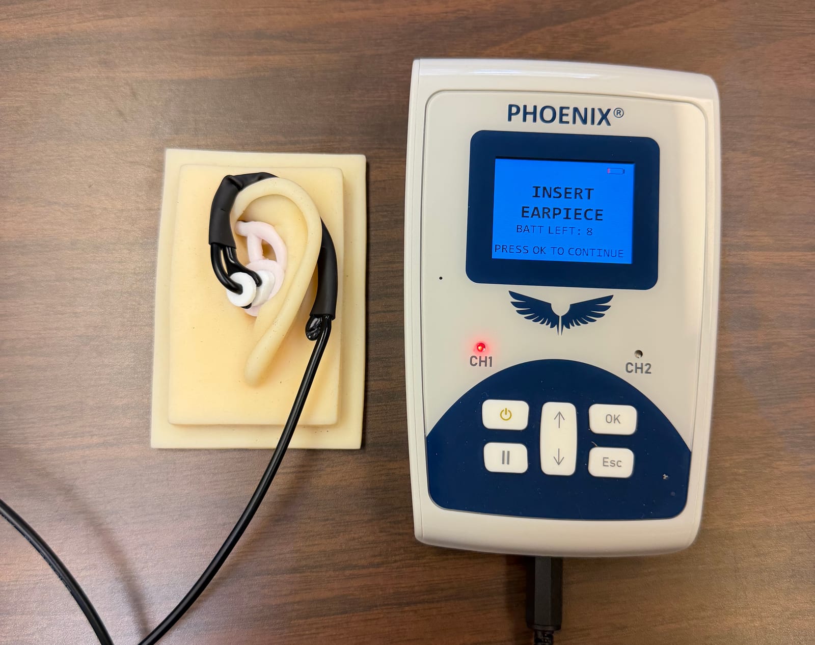 The Evren Phoenix controller beside an assembled ear piece fitted to a silicone ear model